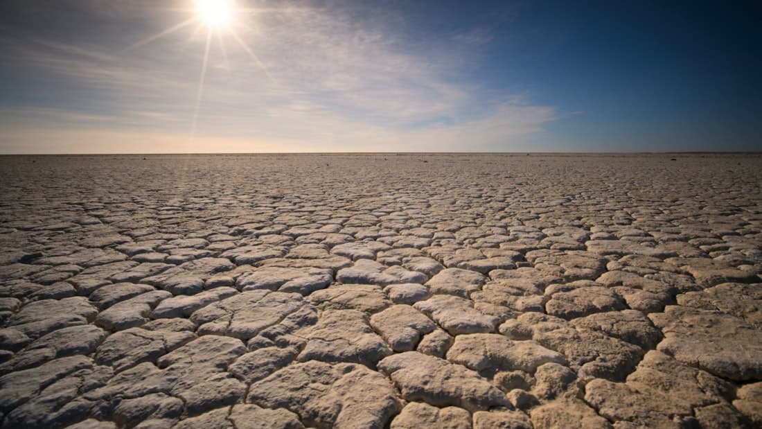 A vast plain of cracked, sun-scorched earth stretching to the horizon under a blazing sun.